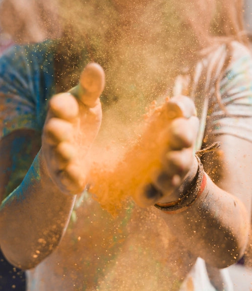 Mains d’une femme libérant une poudre orange et créant une explosion de couleurs, métaphore visuelle de la Gestalt thérapie : mouvement, expression et énergie de transformation.