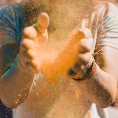 Mains d’une femme libérant une poudre orange et créant une explosion de couleurs, métaphore visuelle de la Gestalt thérapie : mouvement, expression et énergie de transformation.